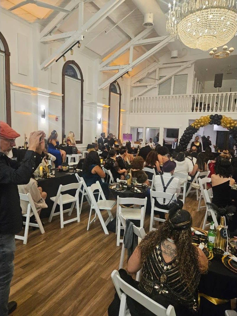 A ballroom filled with seated guests at a formal gala under a chandelier