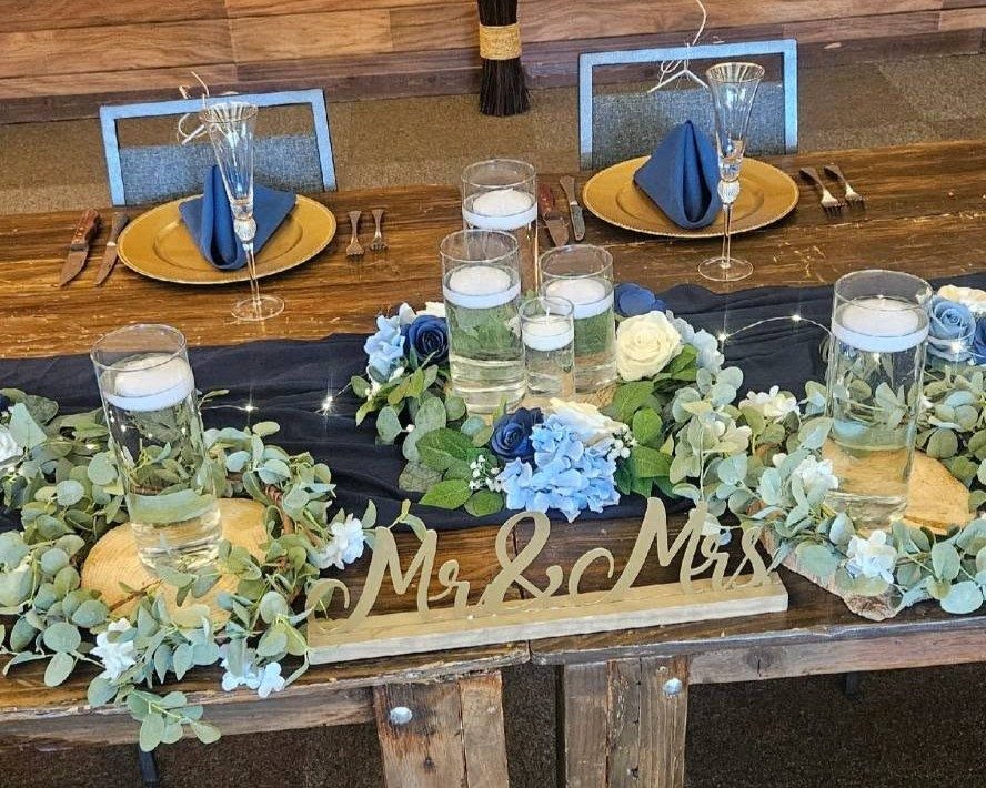 A sweetheart table with floating candles, blue and white florals, and a wooden Mr. and Mrs. sign