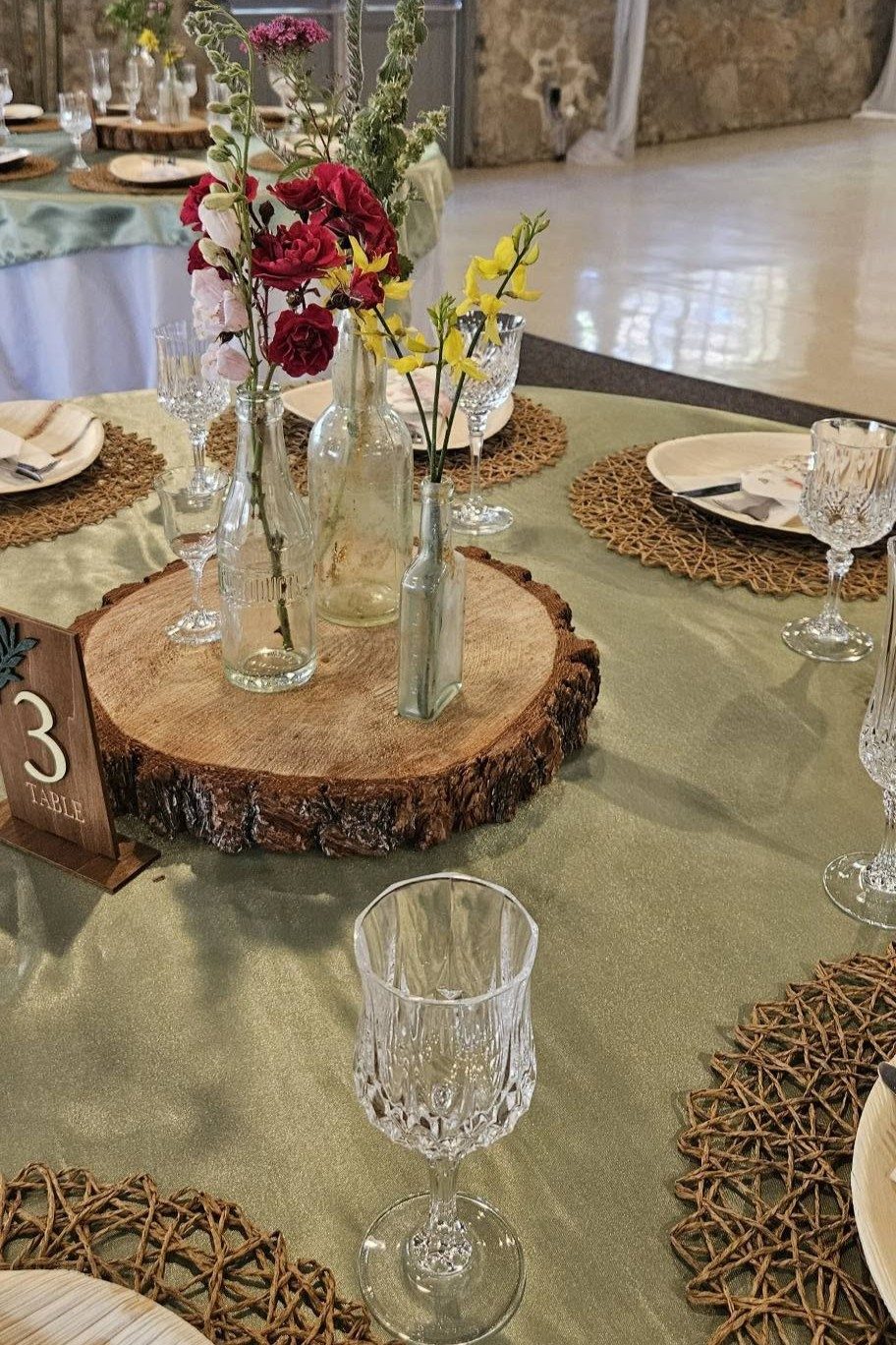 Wildflowers in glass bottles on a wood-slice centerpiece, table number three