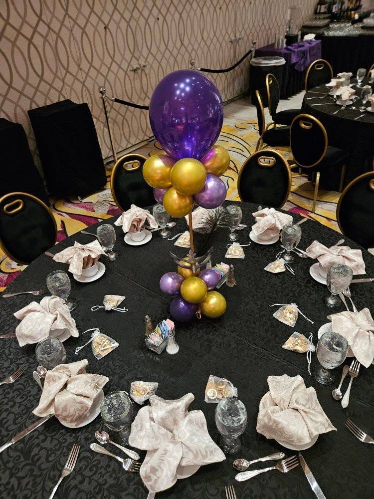 A black, gold, and purple place setting at a formal ballroom gala table