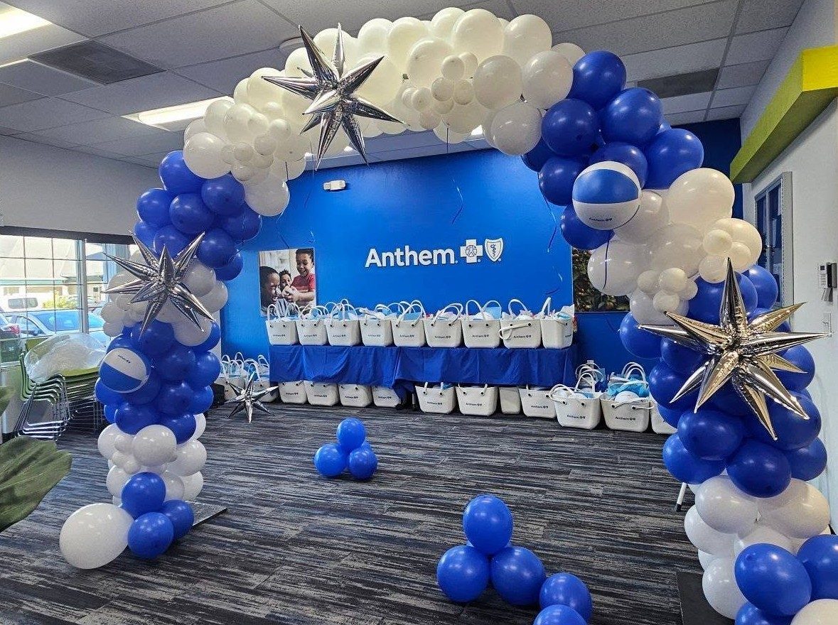 A blue and white balloon arch with silver stars at a corporate brand-launch event, with branded gift bags on tables