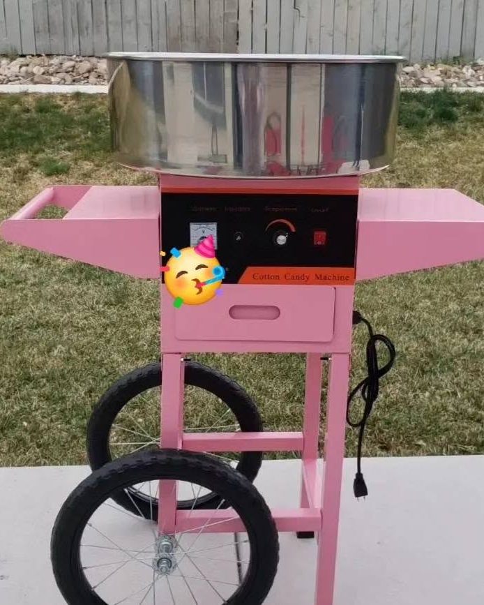 A pink cotton candy cart with a stainless steel spinning bowl, set up on grass at an outdoor event