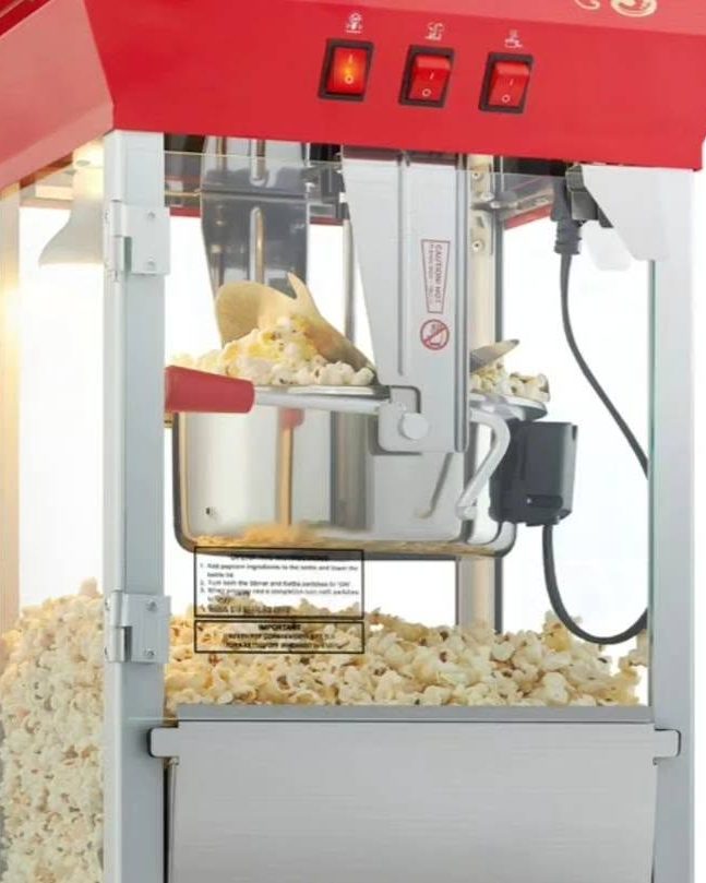 A red-topped popcorn machine with a full kettle and popped corn filling the cabinet